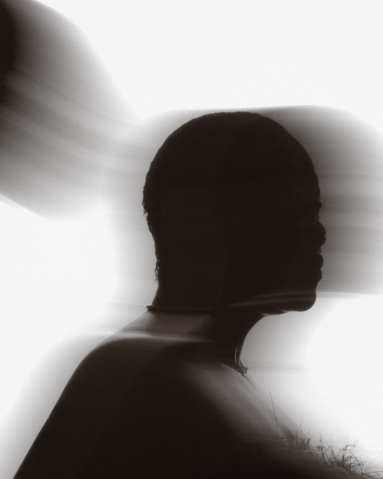 High key and blurred: a bare shoulder and a head doubled by movement against white, more shadow than person