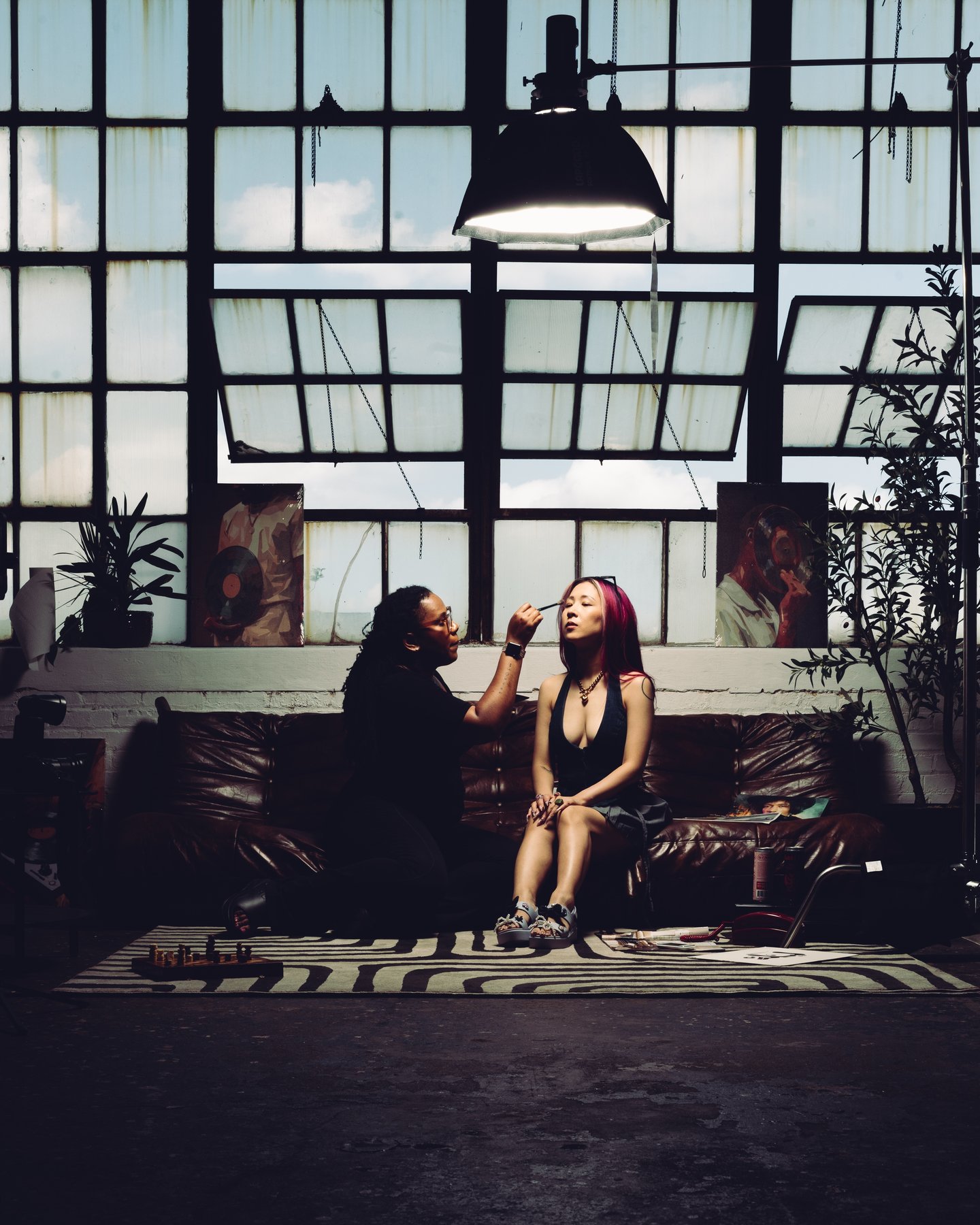 Two women sitting on the striped rug under the loft windows, one drinking from a can
