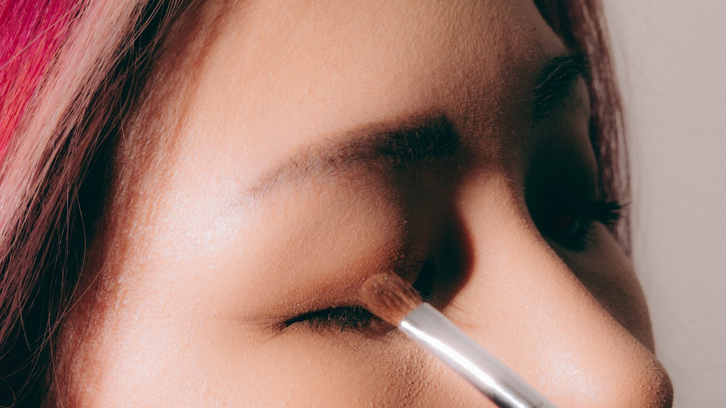 A close crop of closed eyes and a gloss applicator in warm light