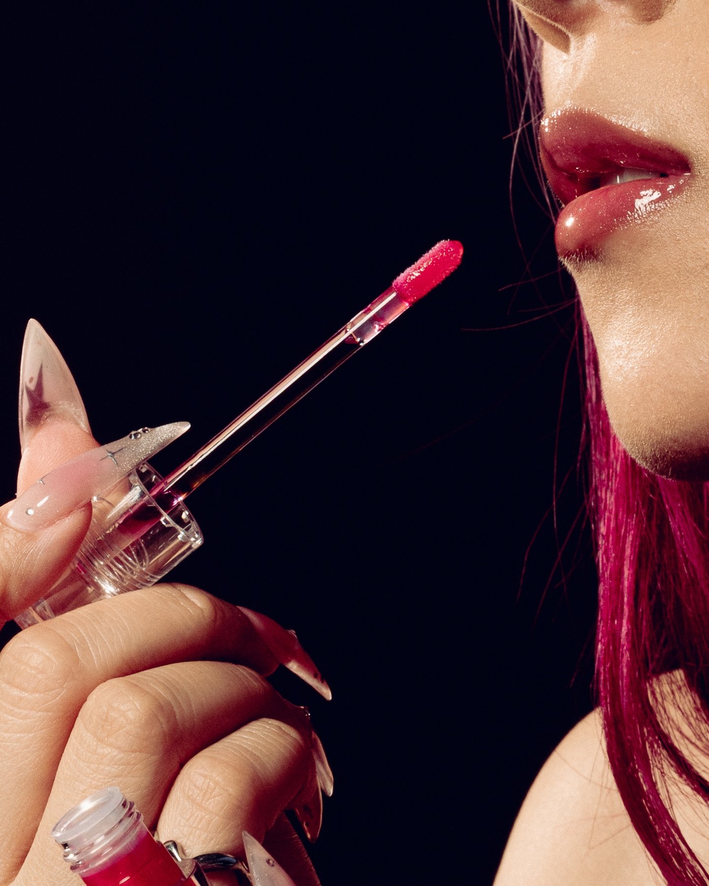 Close on a gloss wand at glossy lips, red tipped nails