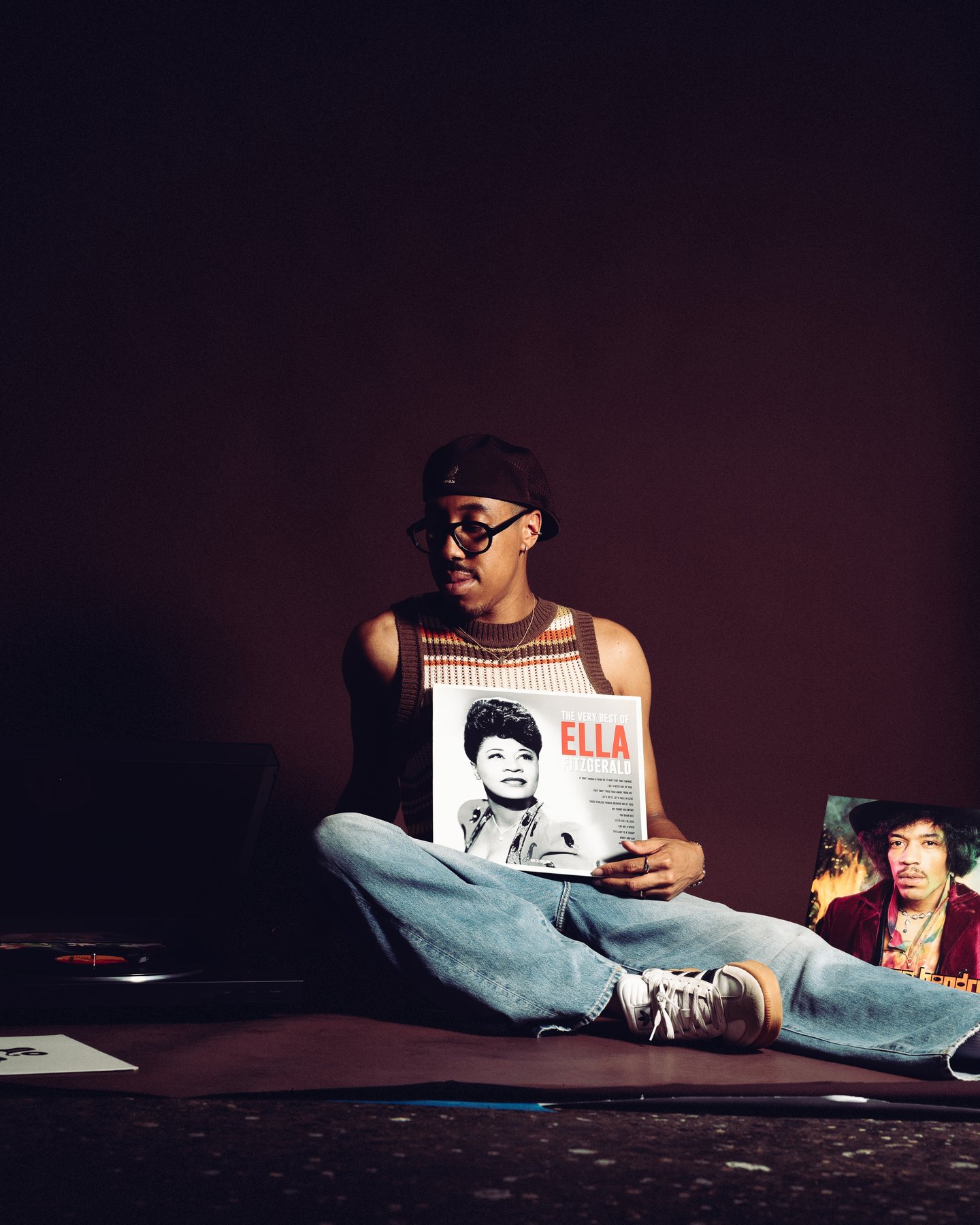 Kyle sitting cross legged on the sofa in headphones, holding an Ella record sleeve