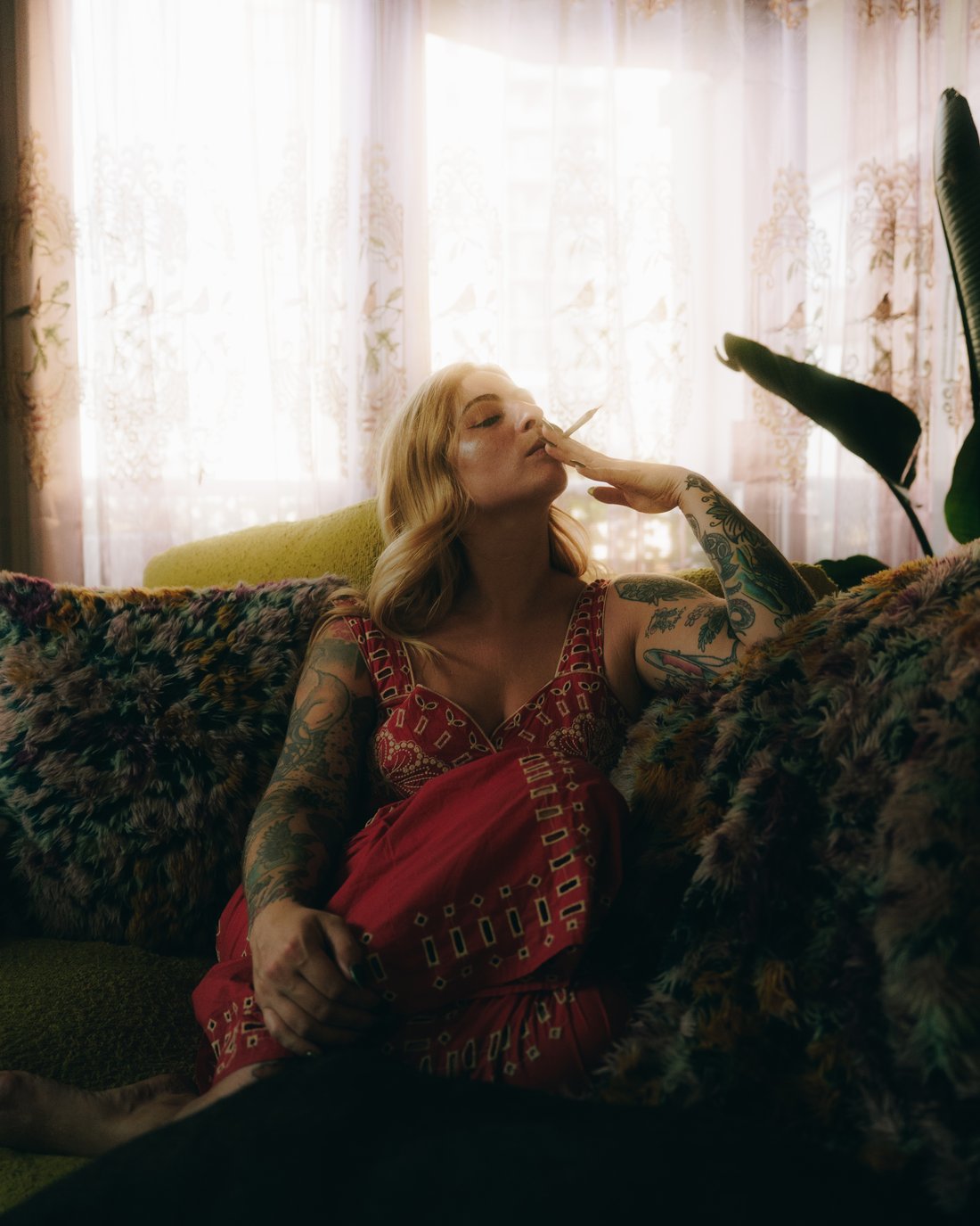 A woman reclining on a fur throw with her legs kicked up, backlit by sheer curtains