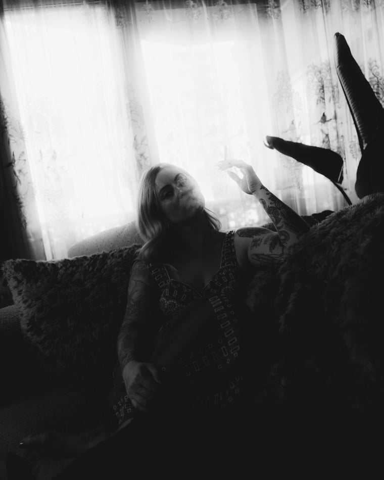 Black and white and blurred: heeled boots kicked up in front of a bright curtained window