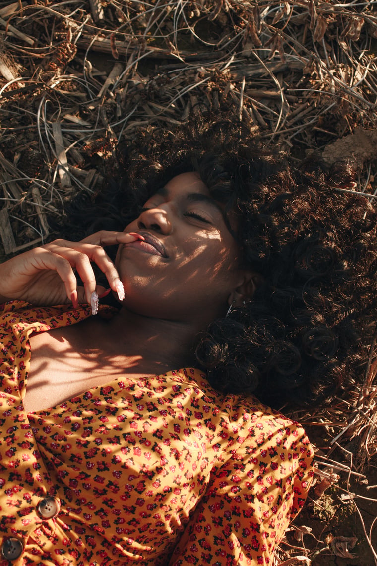 The same woman lying back in the dry stalks, sunlight cutting in bands across her face