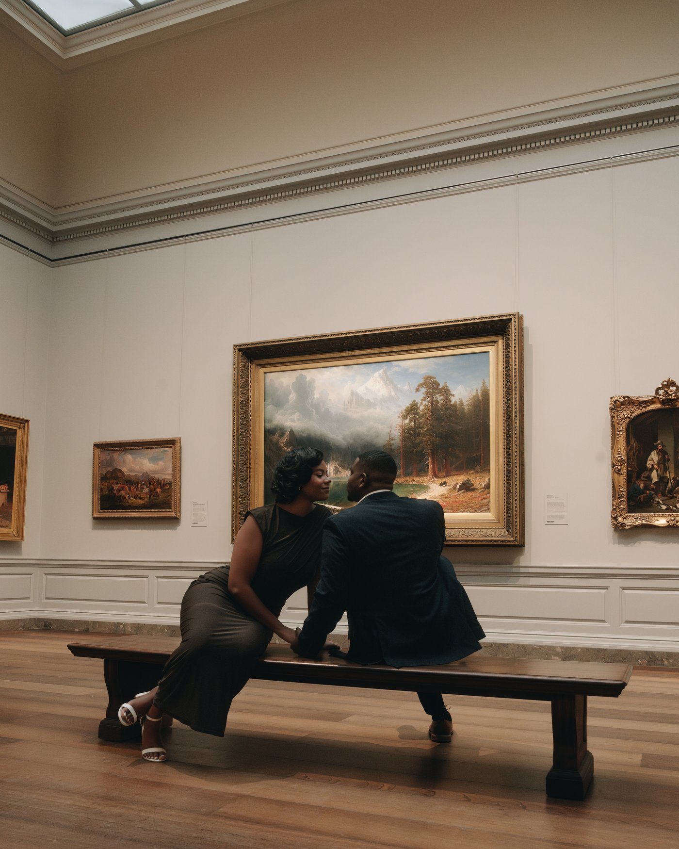 A couple leaning into each other on a wooden bench in front of a landscape painting