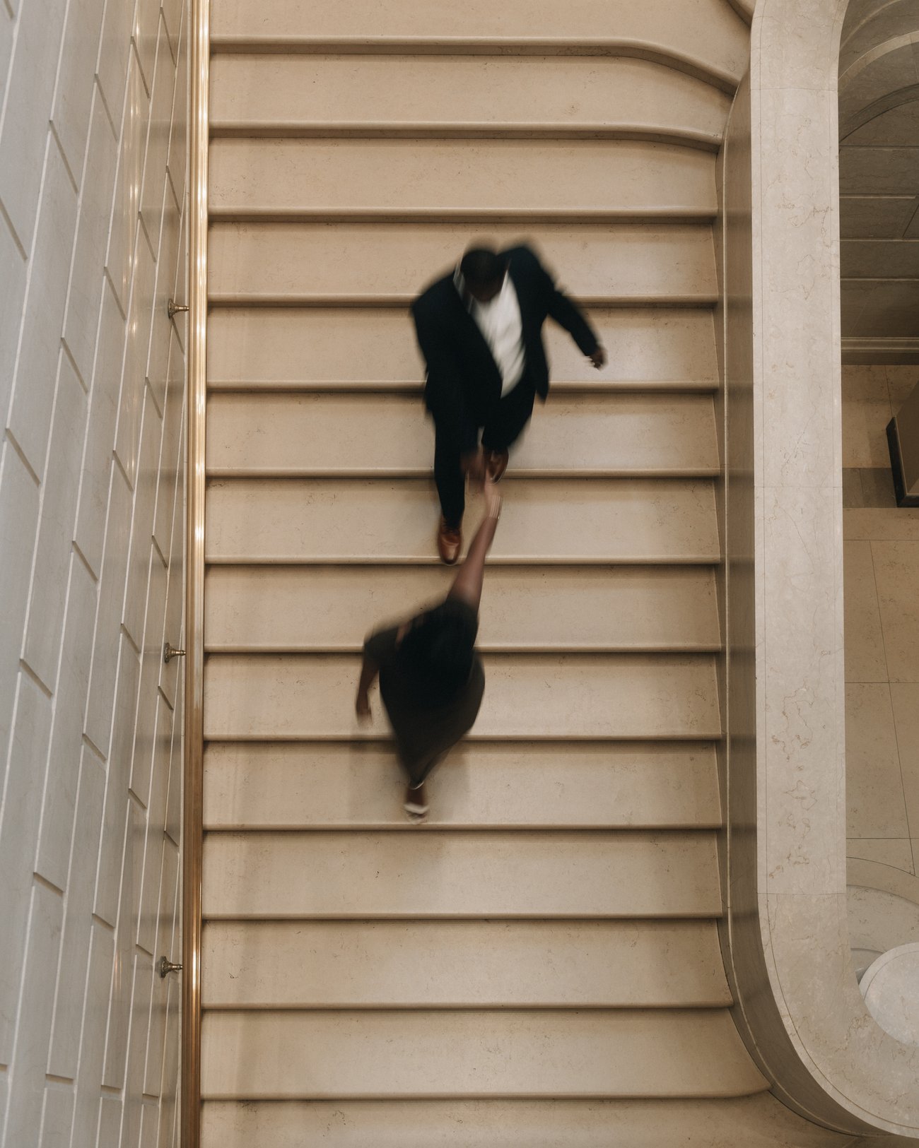 Looking straight down a curving stone staircase as a couple run up it, both blurred by the movement