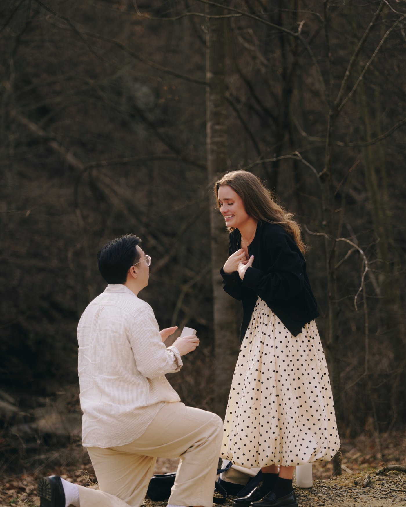 One of them down on a knee in the winter woods holding out the ring, the other with a hand at her chest