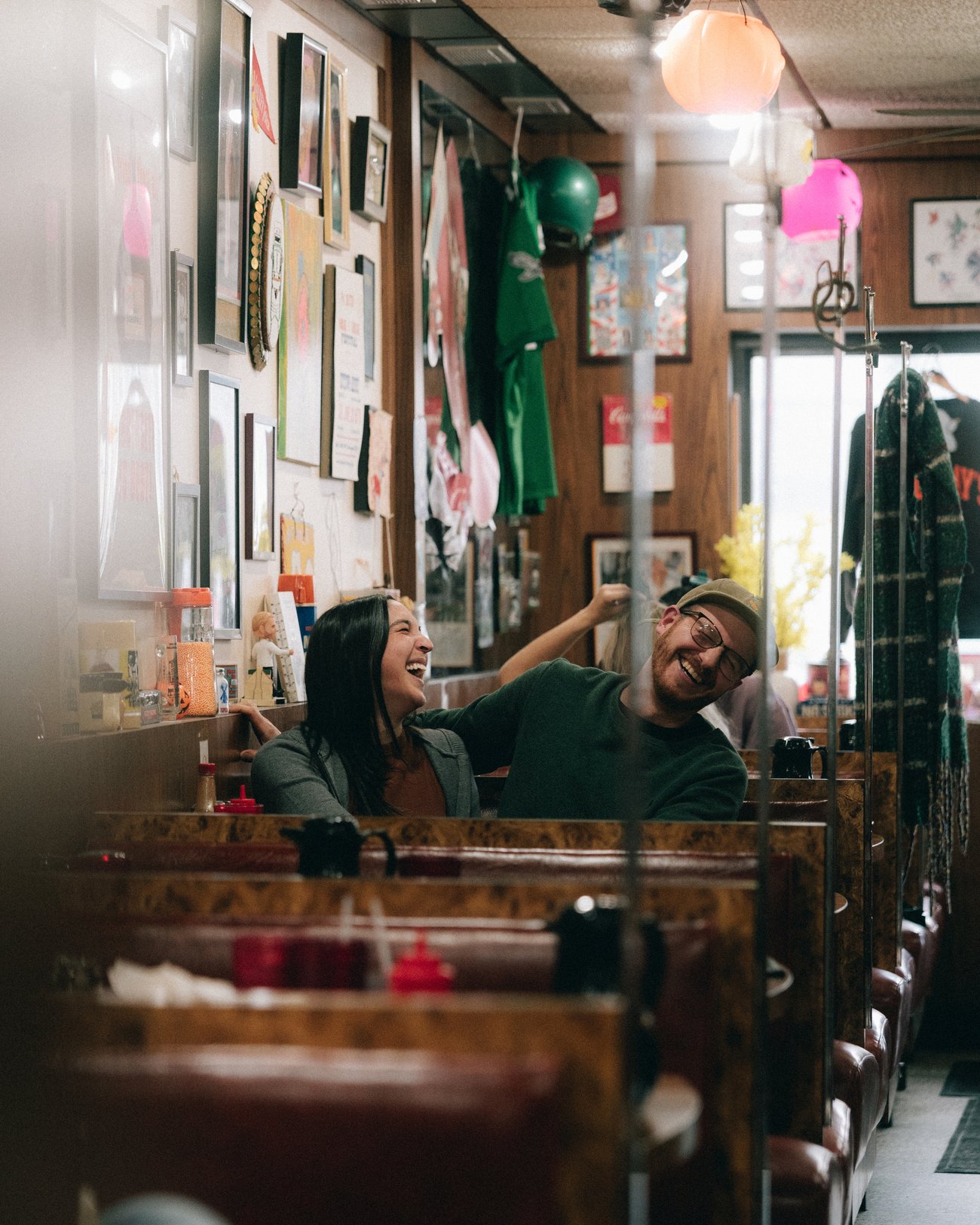 A couple laughing across the table of a diner booth, the walls behind them covered in framed pictures
