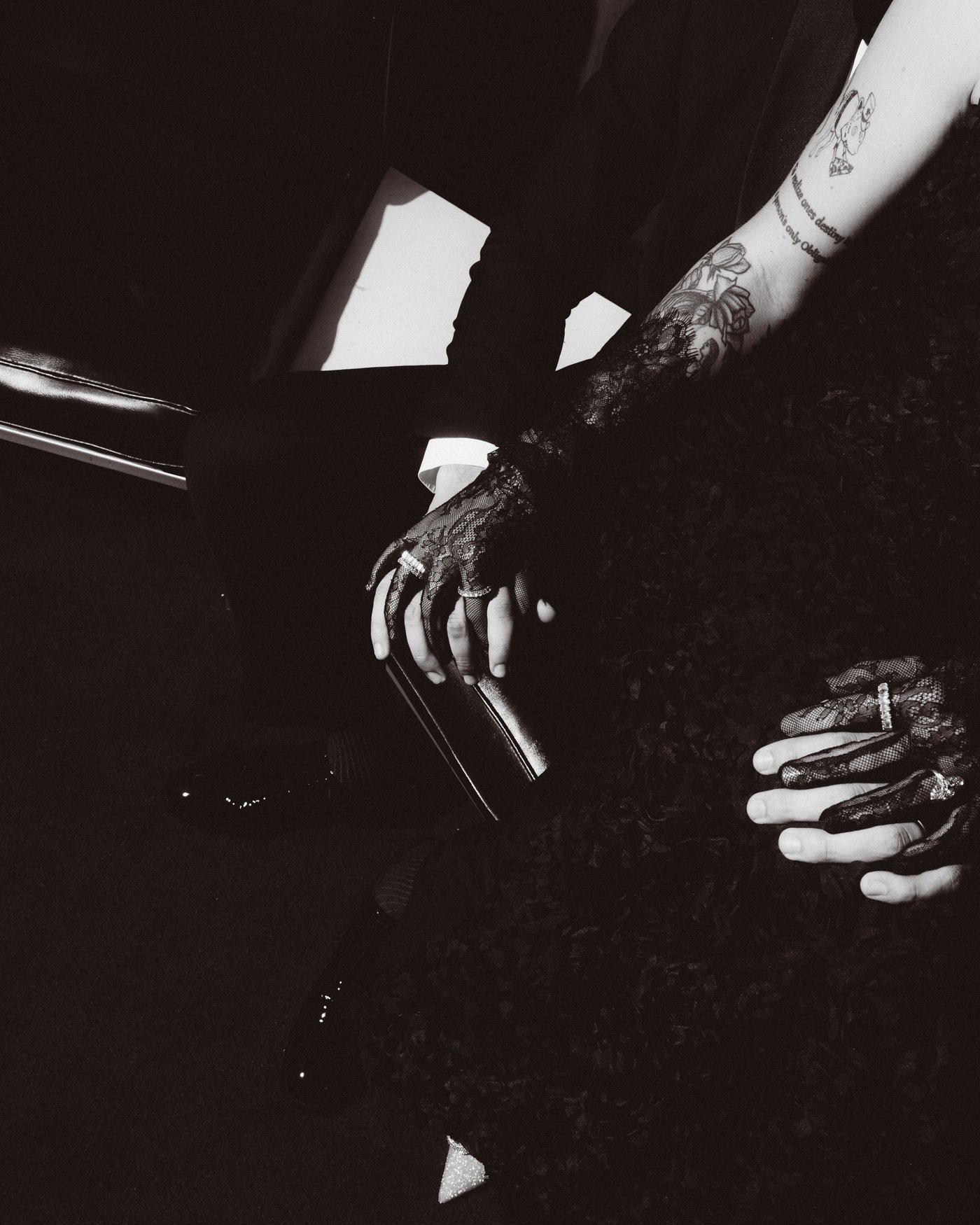 Two hands resting on a dark table in near darkness, one arm tattooed, a ring catching the last of the light