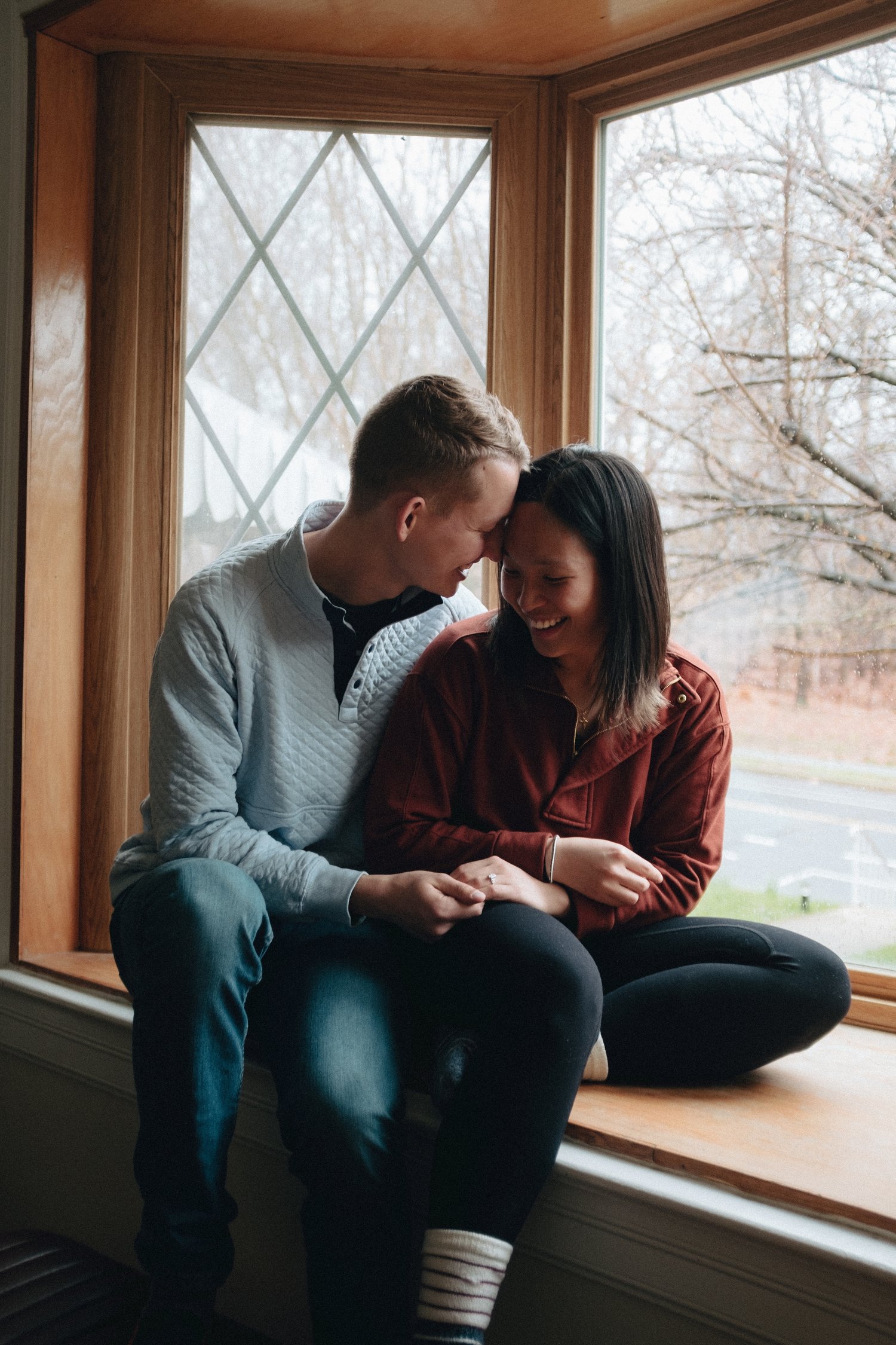 Cross legged on the cushion of a bay window, foreheads together, hands held between them