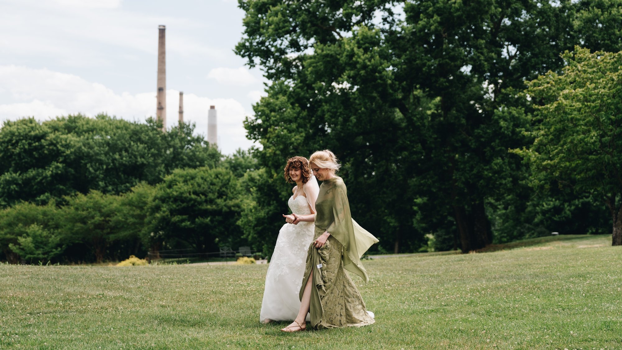 The bride walking across the lawn in her gown, a guest in green beside her