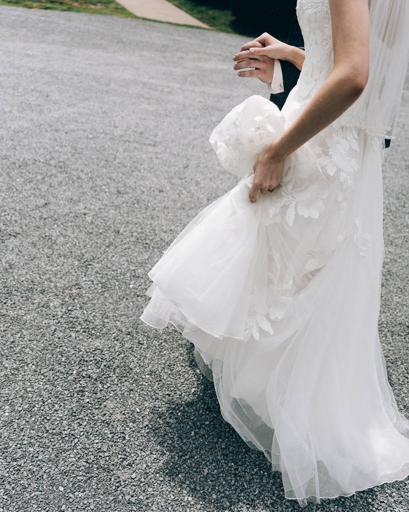 The bride's gown and train trailing across the gravel drive