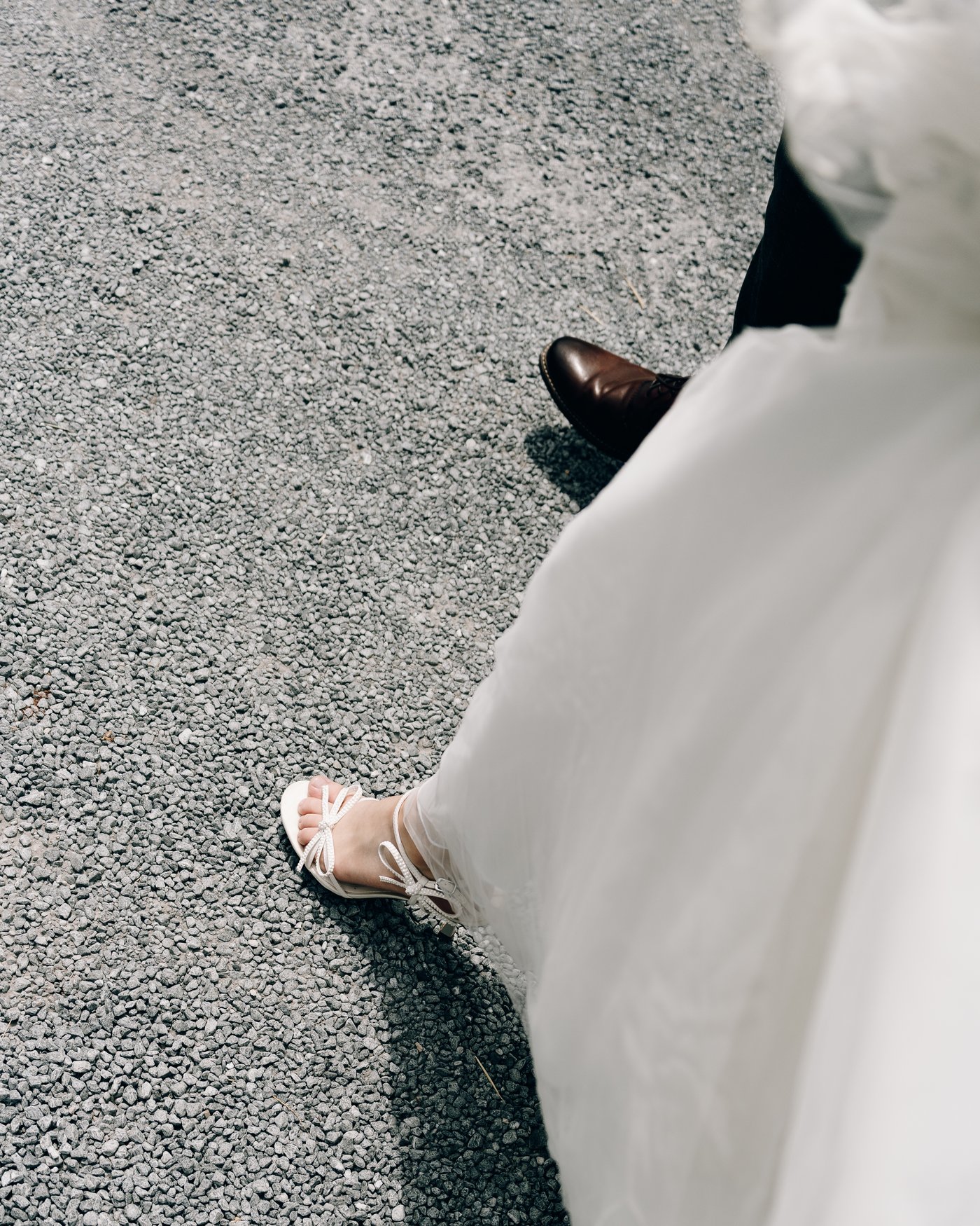 The hem of the bride's gown and her shoe on the gravel