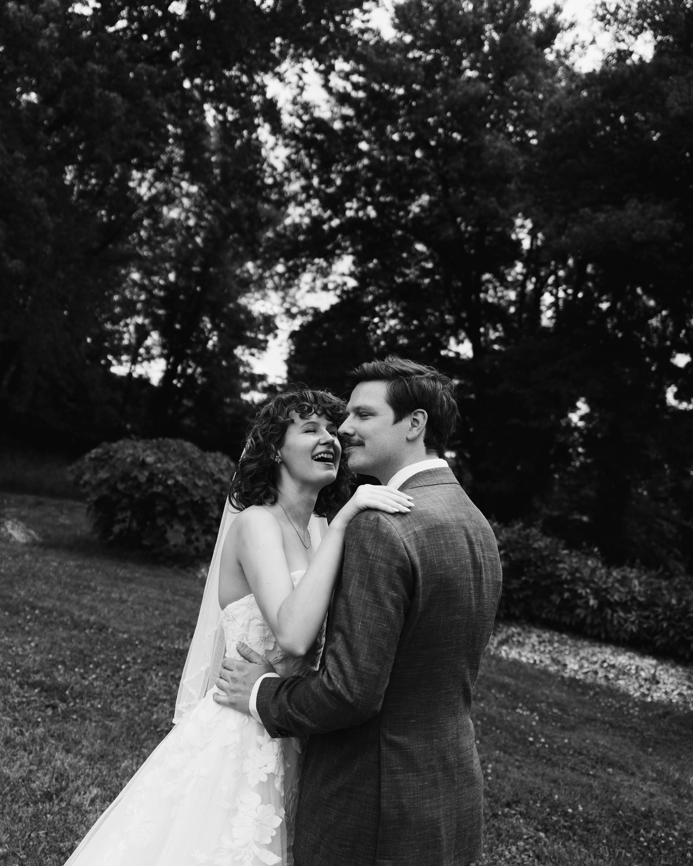 Black and white, the bride and groom close together with the trees behind them