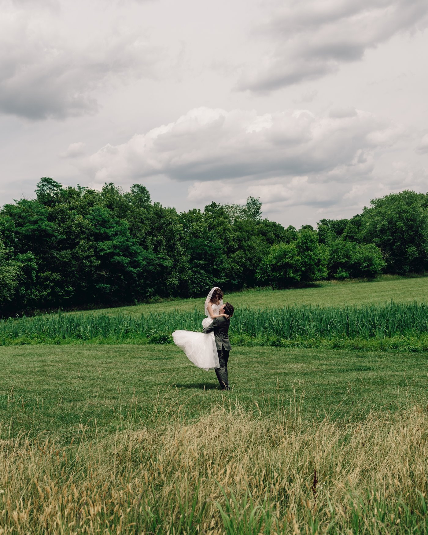 The groom lifting the bride off her feet in the long grass at the top of the property