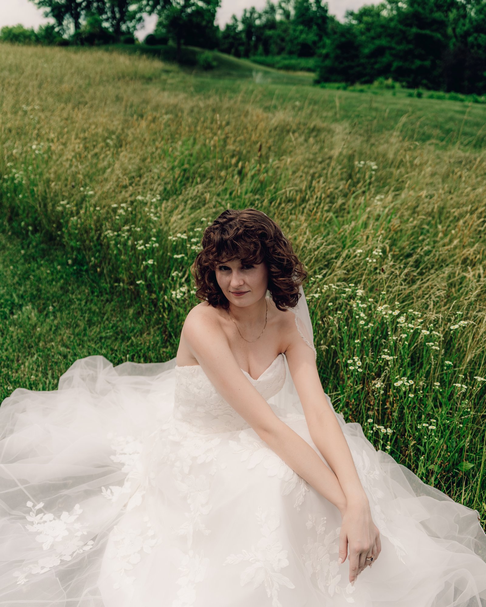 The bride sitting in the grass with her gown spread out around her