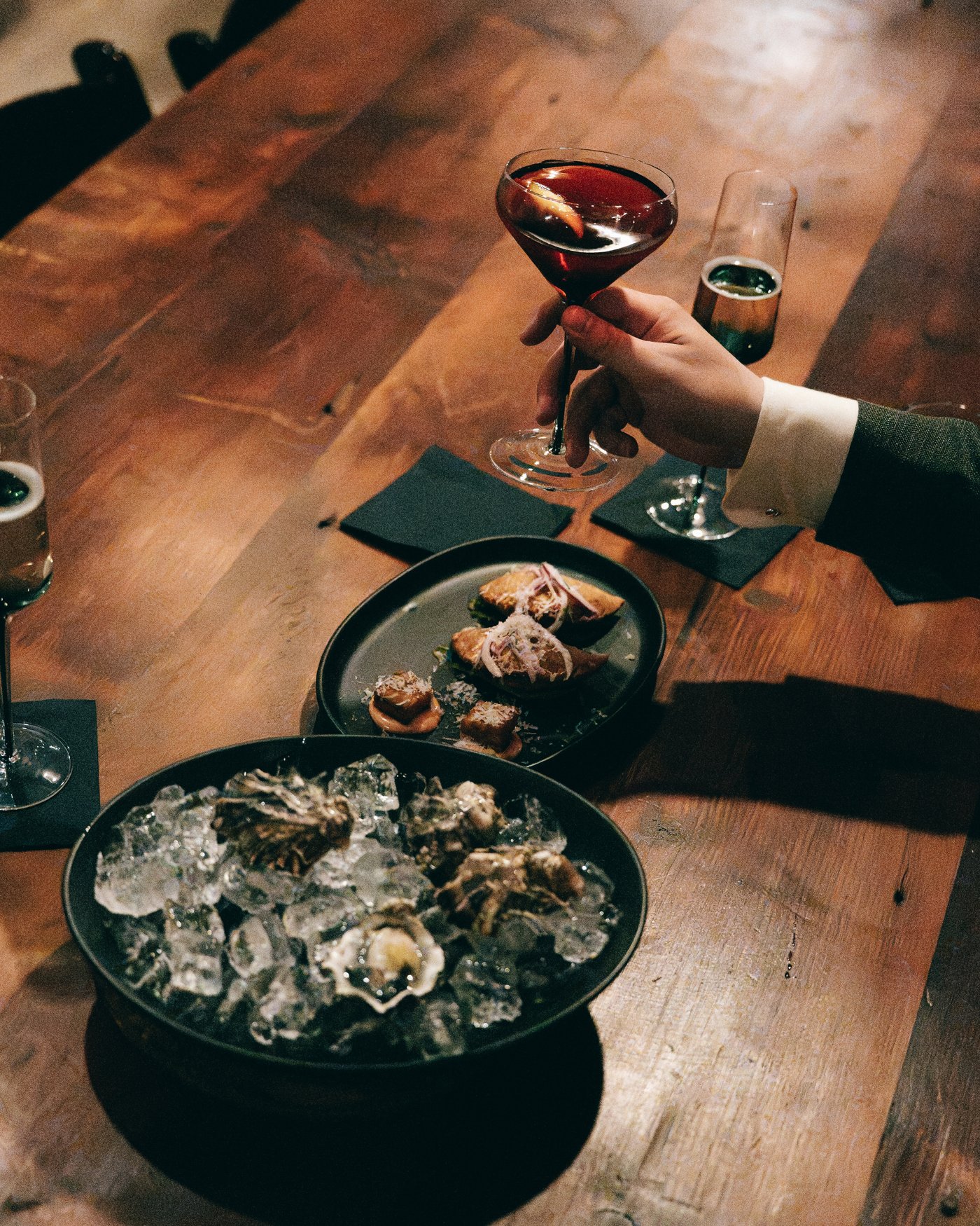 A coupe glass raised over trays of oysters on a dark wooden table