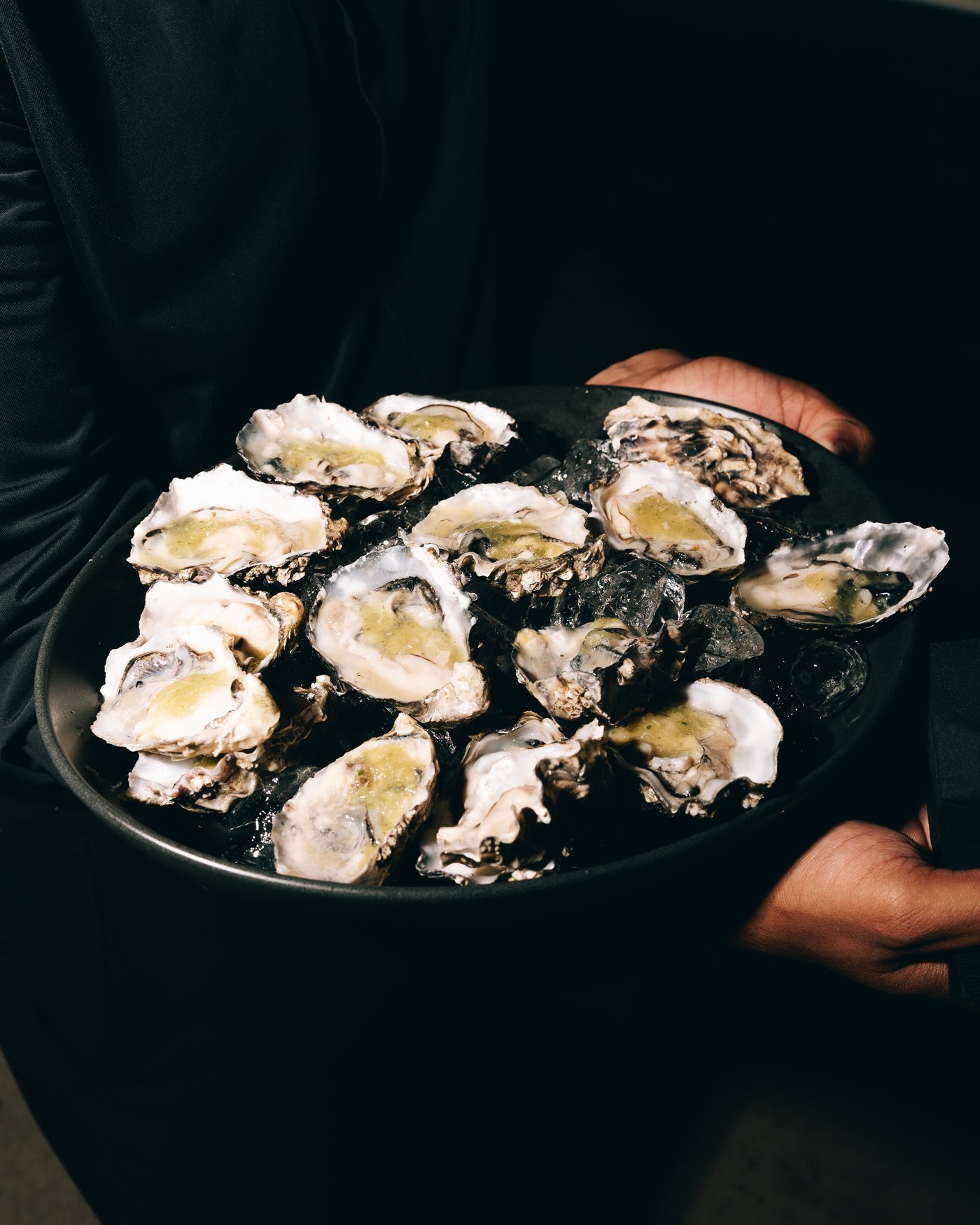 A tray of oysters on ice held up in the dark