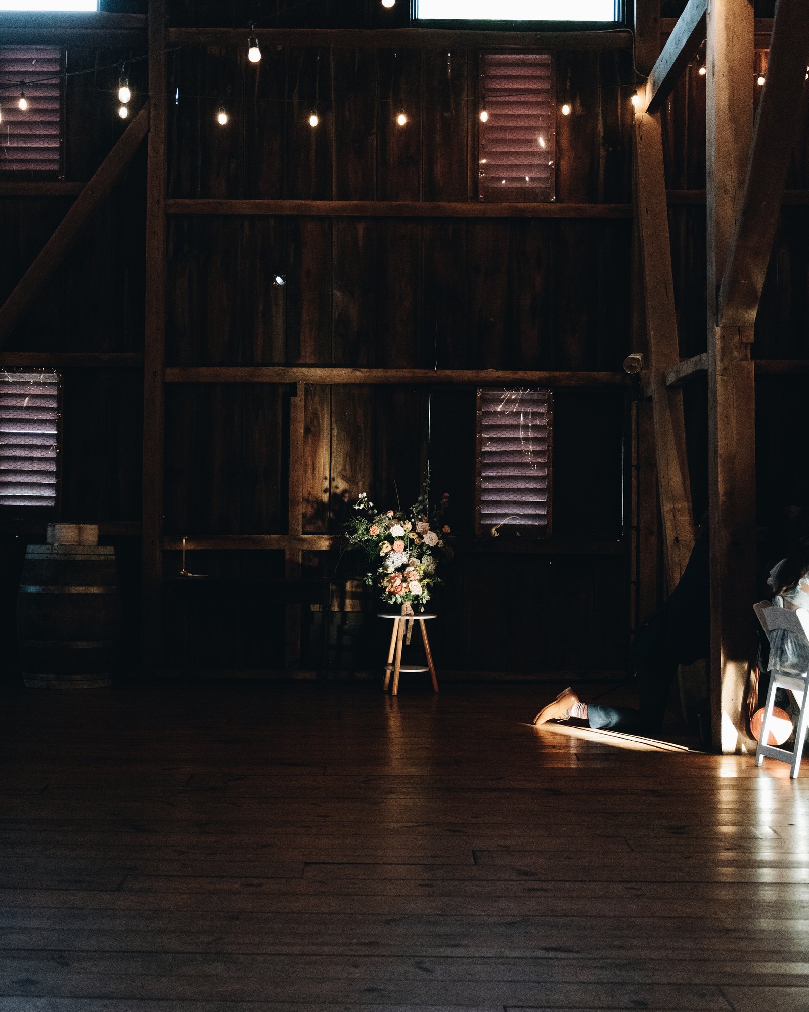 The empty barn floor at night, a single arrangement of flowers on a stool in the light