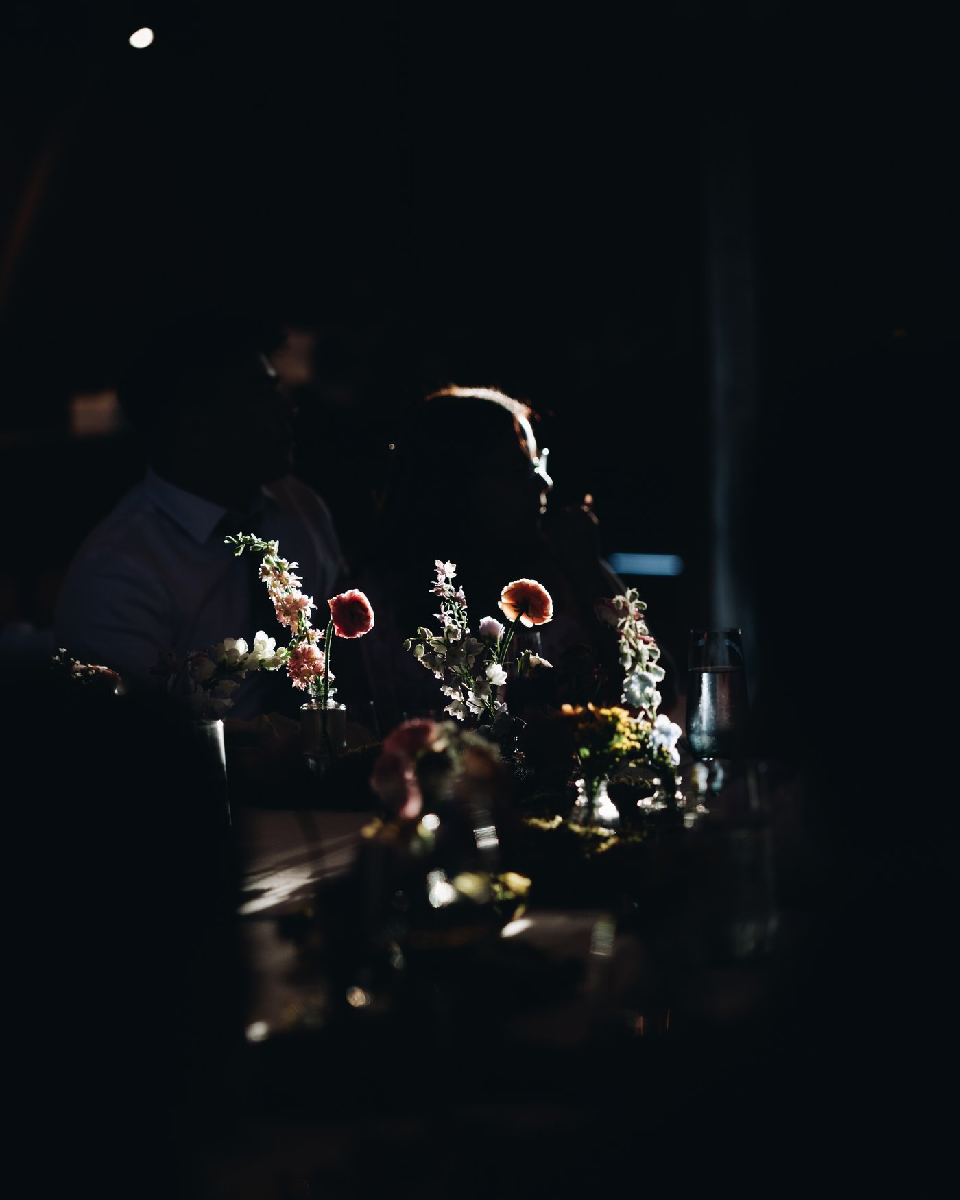 Wildflowers on the table in near darkness with guests behind them