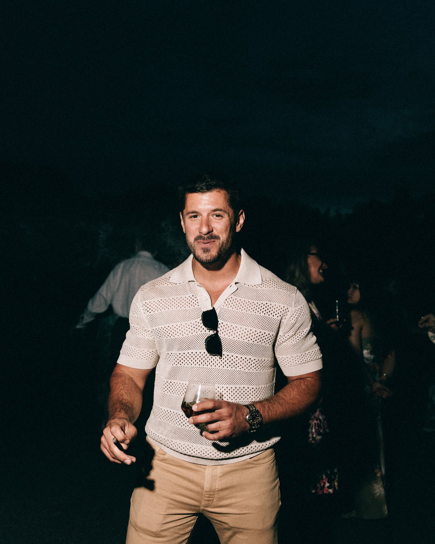 A guest holding a drink on the lawn after dark