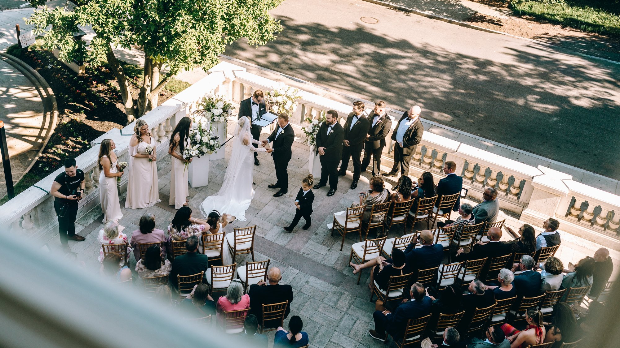 The ceremony from the balcony above, the wedding party fanned out to either side and a ring bearer crossing the stones