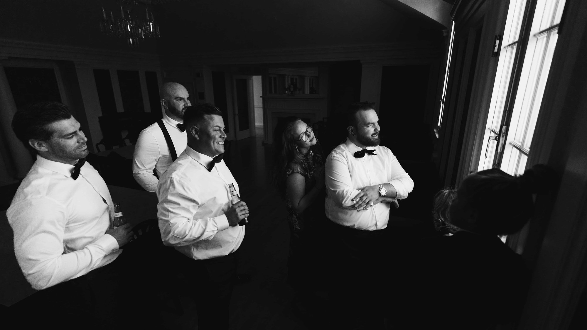 Black and white, the wedding party watching from a dark room, faces lit by the bright terrace windows