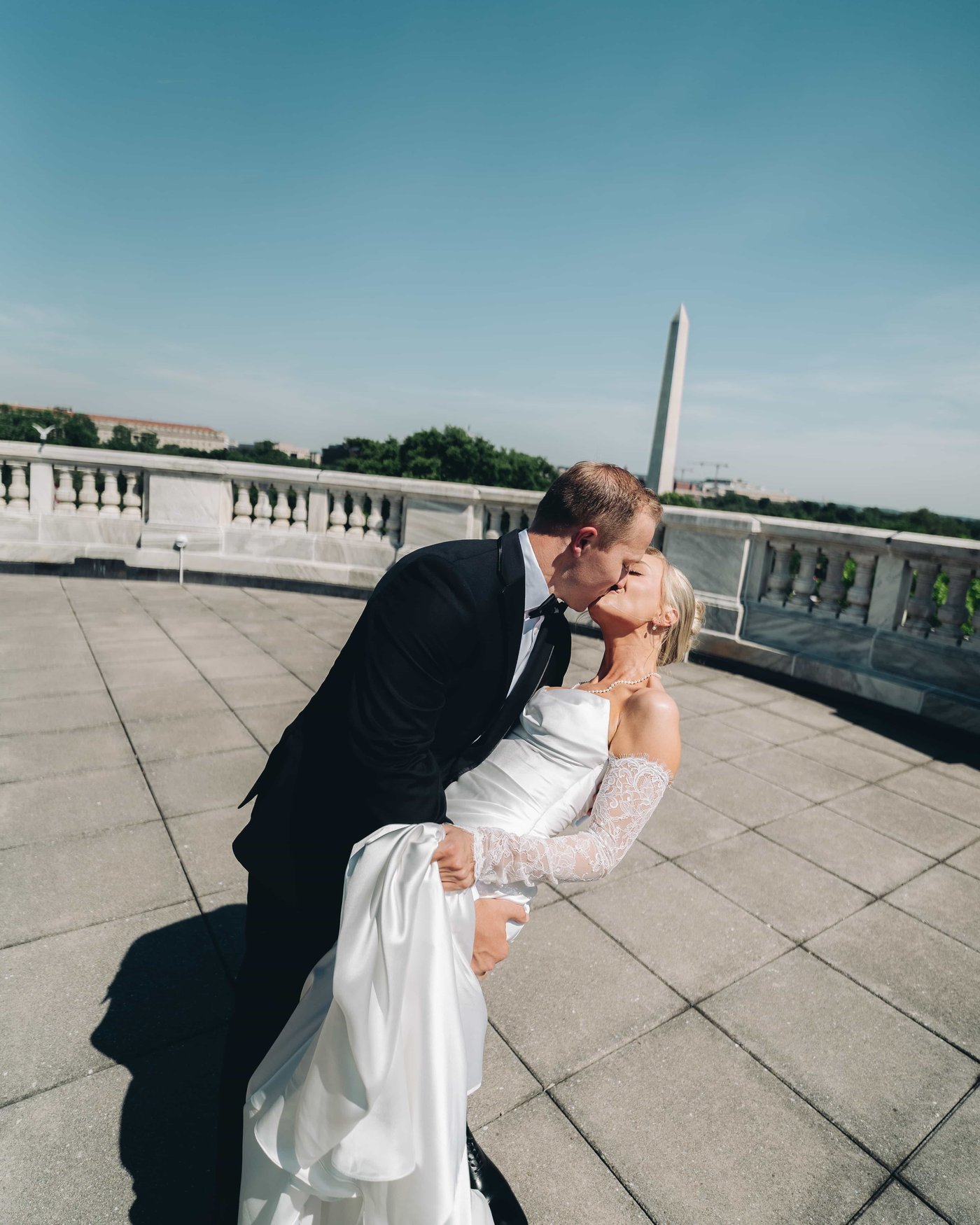 The groom dipping the bride into a kiss on the terrace, the Monument rising behind them