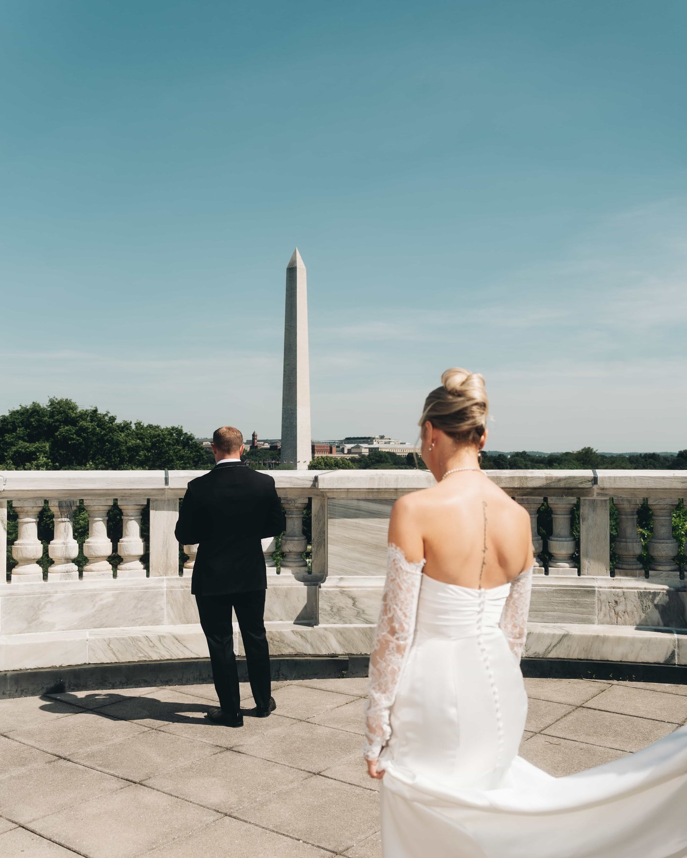 The bride crossing the terrace toward the groom's turned back, the Monument waiting in the distance