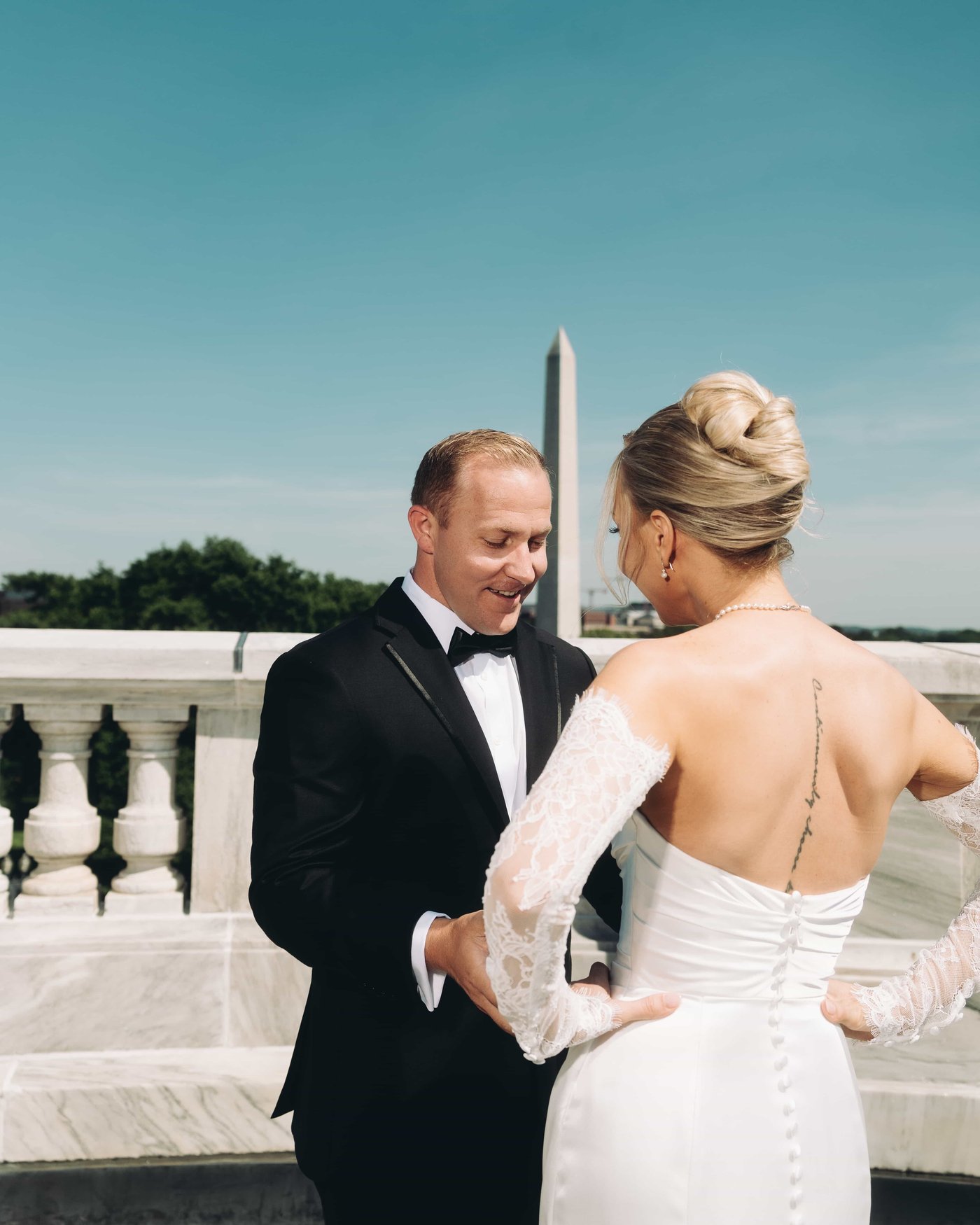 He has just turned, the groom grinning at the bride, her hands resting on her hips in lace sleeves