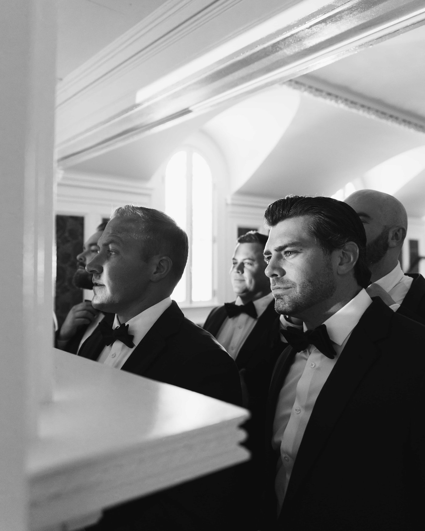 Black and white, the groomsmen lined up in profile at the window, waiting shoulder to shoulder