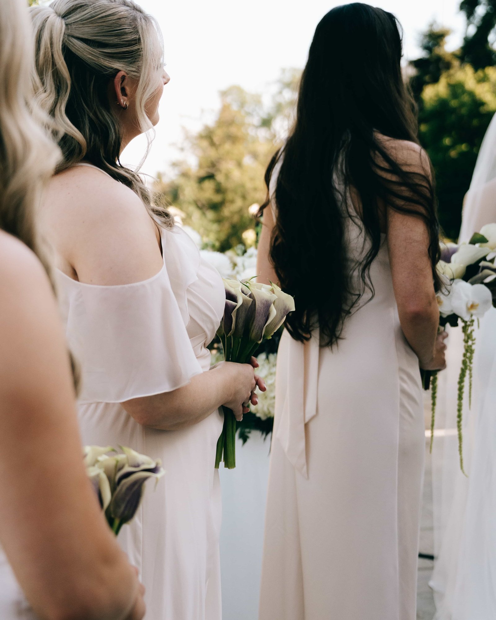 Bridesmaids holding bouquets of purple and white calla lilies, an orchid bouquet at the edge of the frame