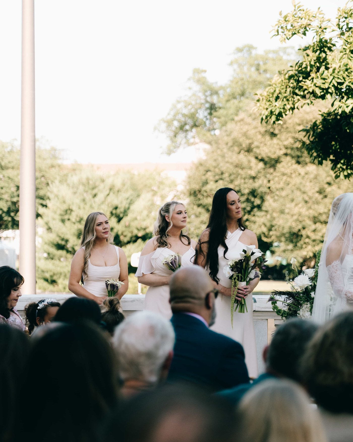 Three bridesmaids standing with their bouquets during the ceremony, guests seated in the foreground