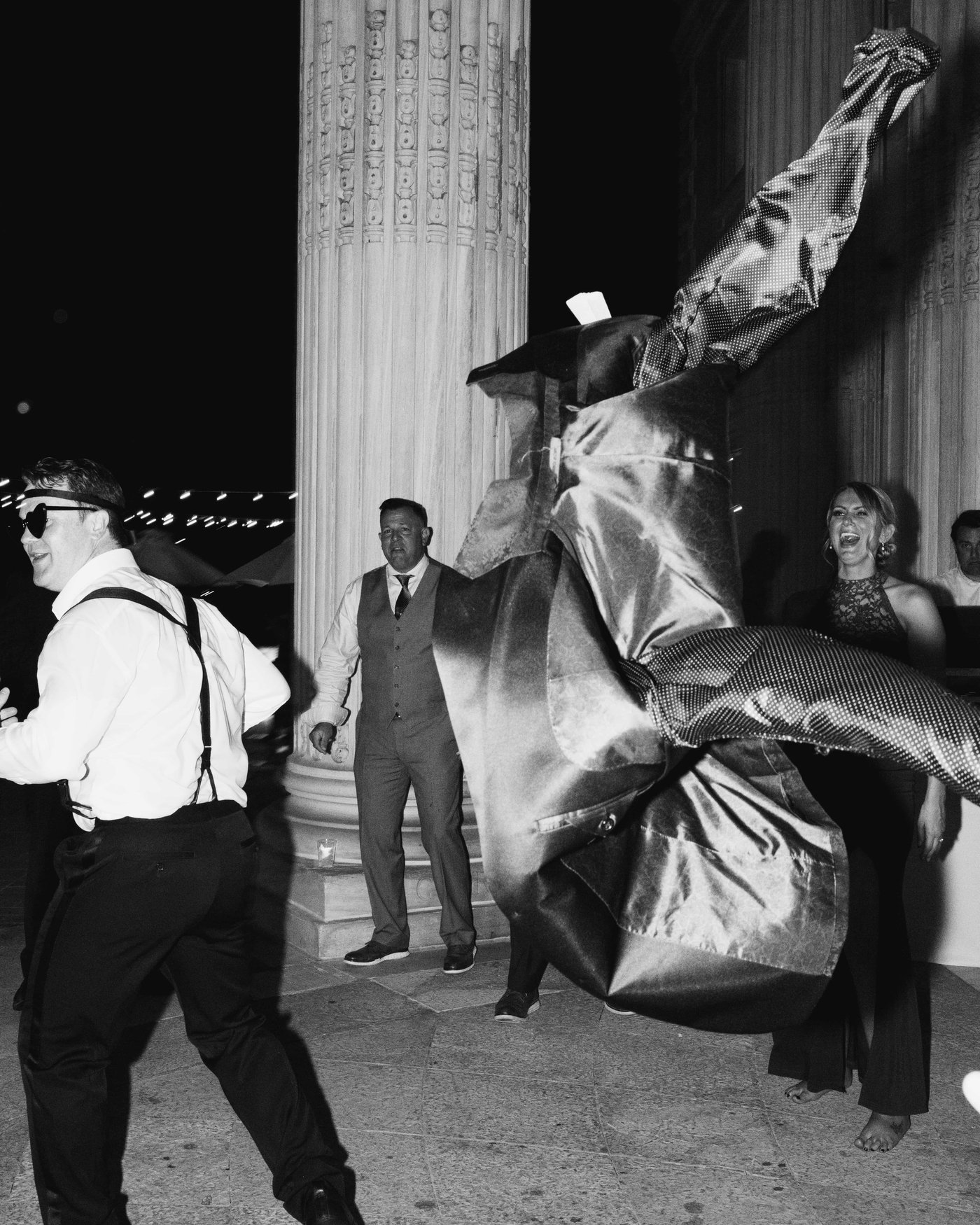 Black and white, a suit jacket flung high across the dance floor, a dancer in suspenders mid stride beneath the columns