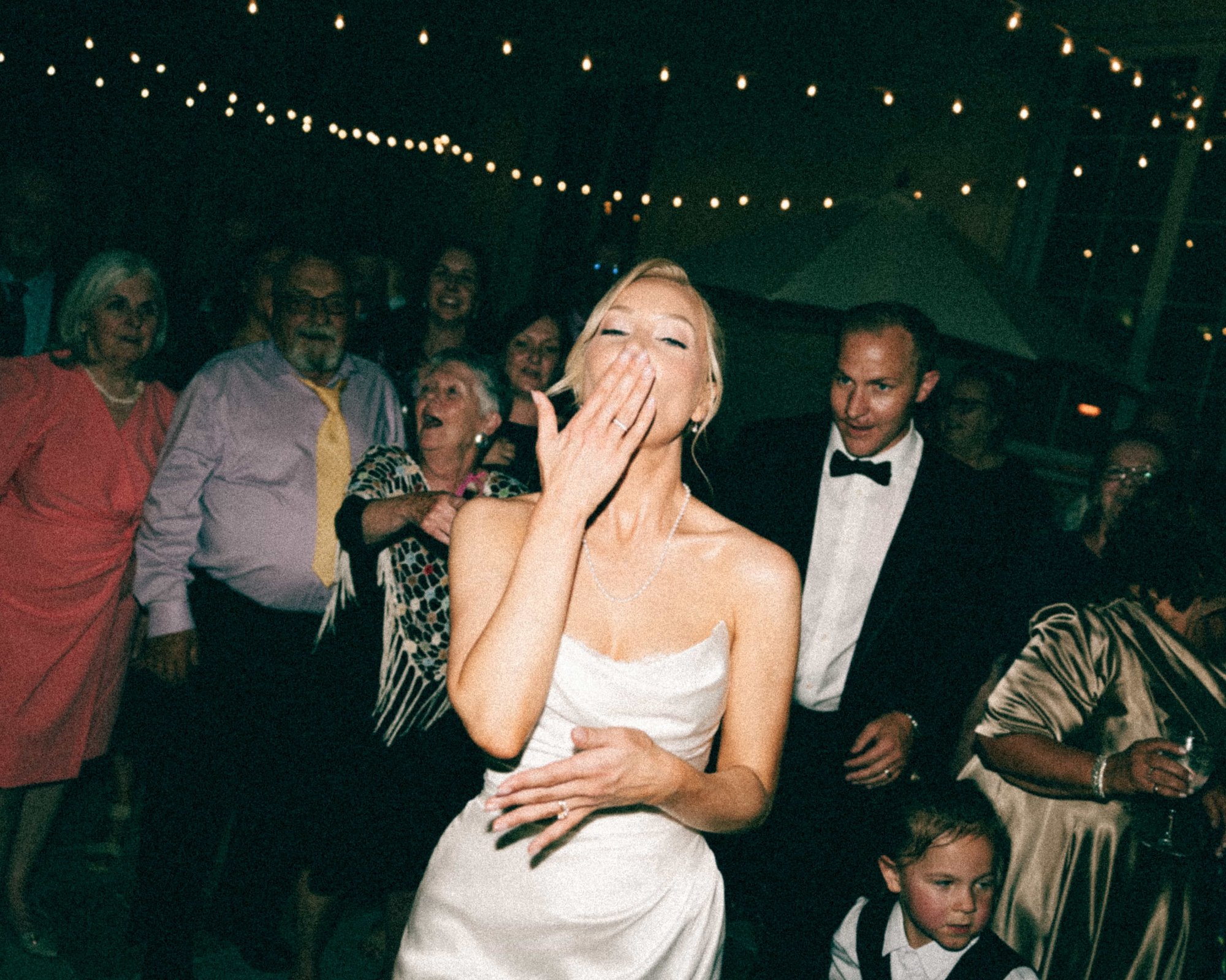 The bride blowing a kiss under the string lights, the whole dance floor lit up behind her