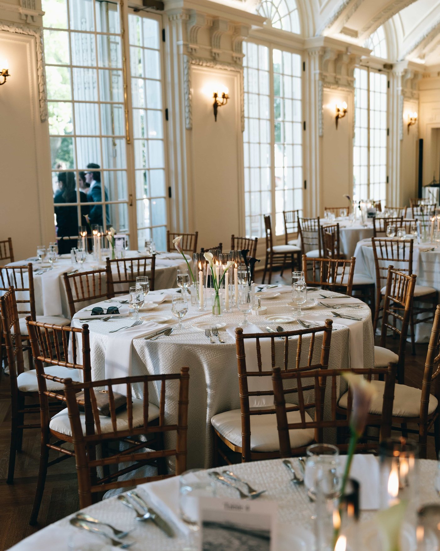 Round tables dressed in white with callas and taper candles, the tall arched windows glowing behind them