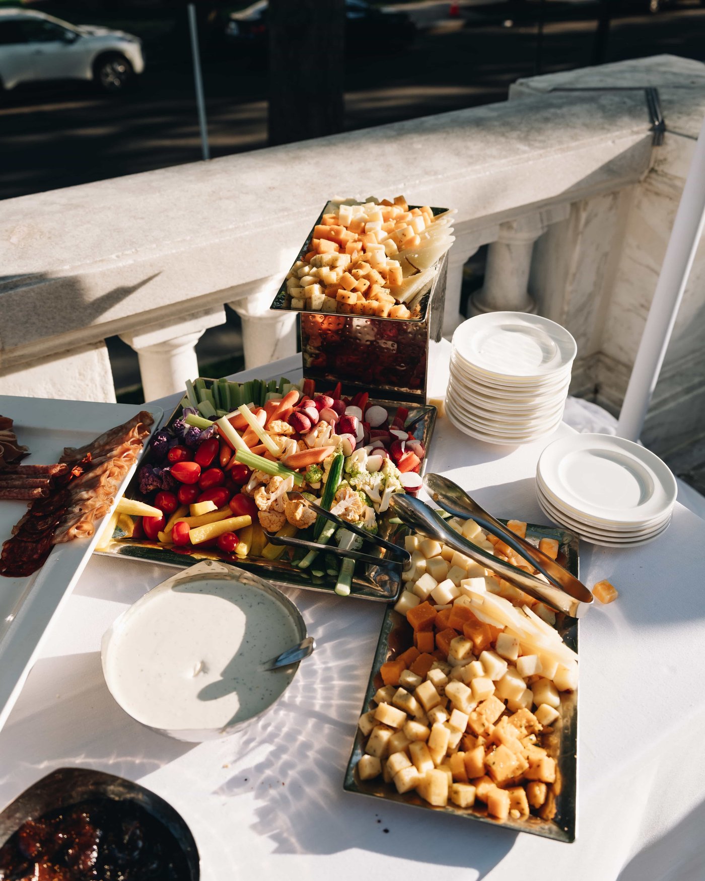 Trays of cheese, crudites and cured meats laid out along the balustrade, stacked plates catching the sun