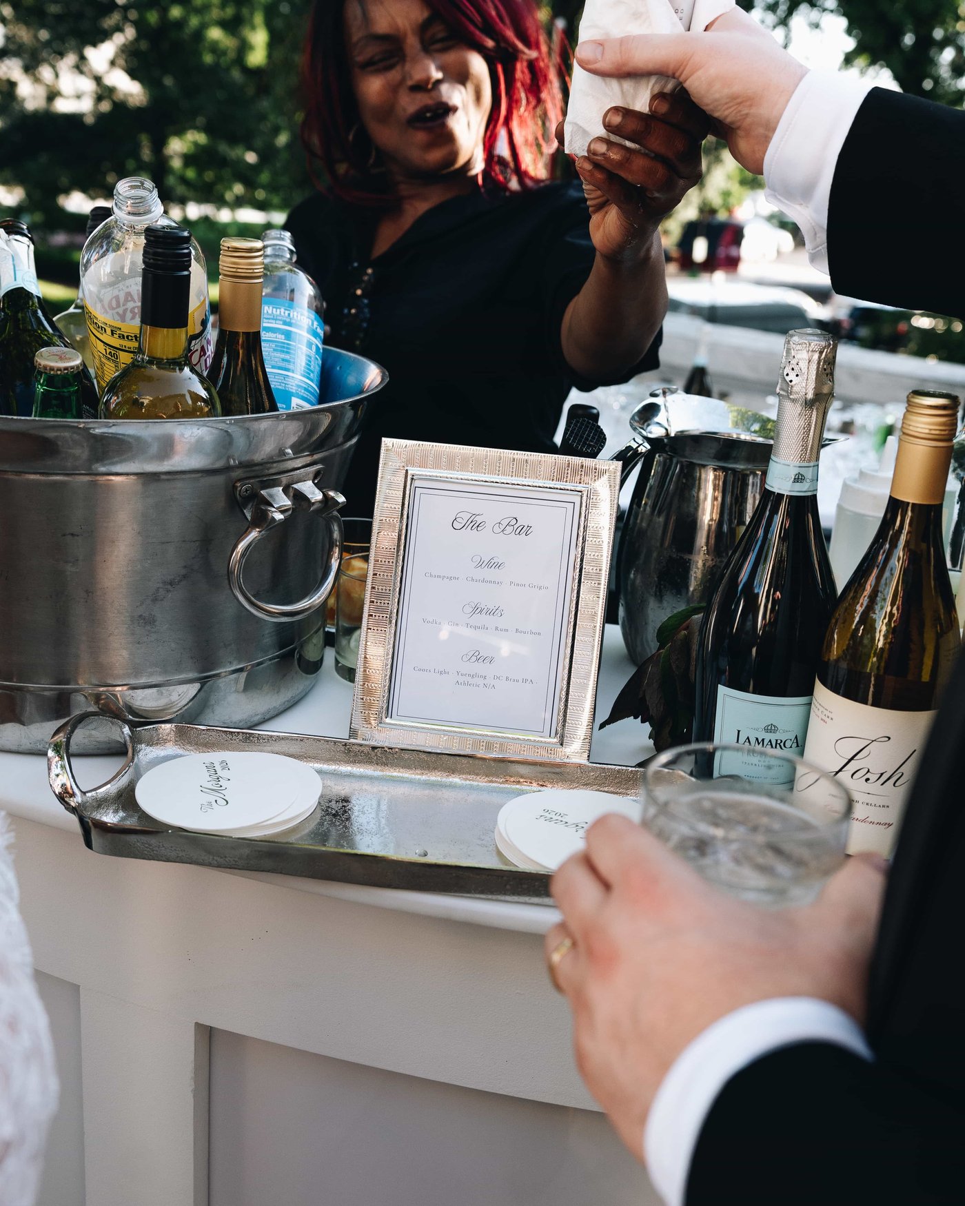 A drink handed across the bar cart, a framed menu propped among the bottles and silver trays