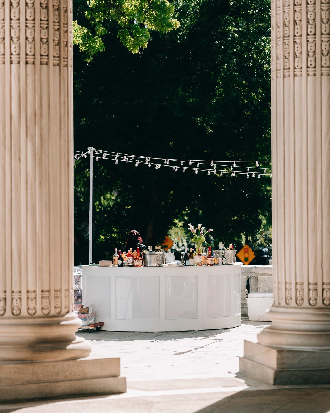 The bar glimpsed between two columns, bottles and flowers laid out under string lights against the dark trees