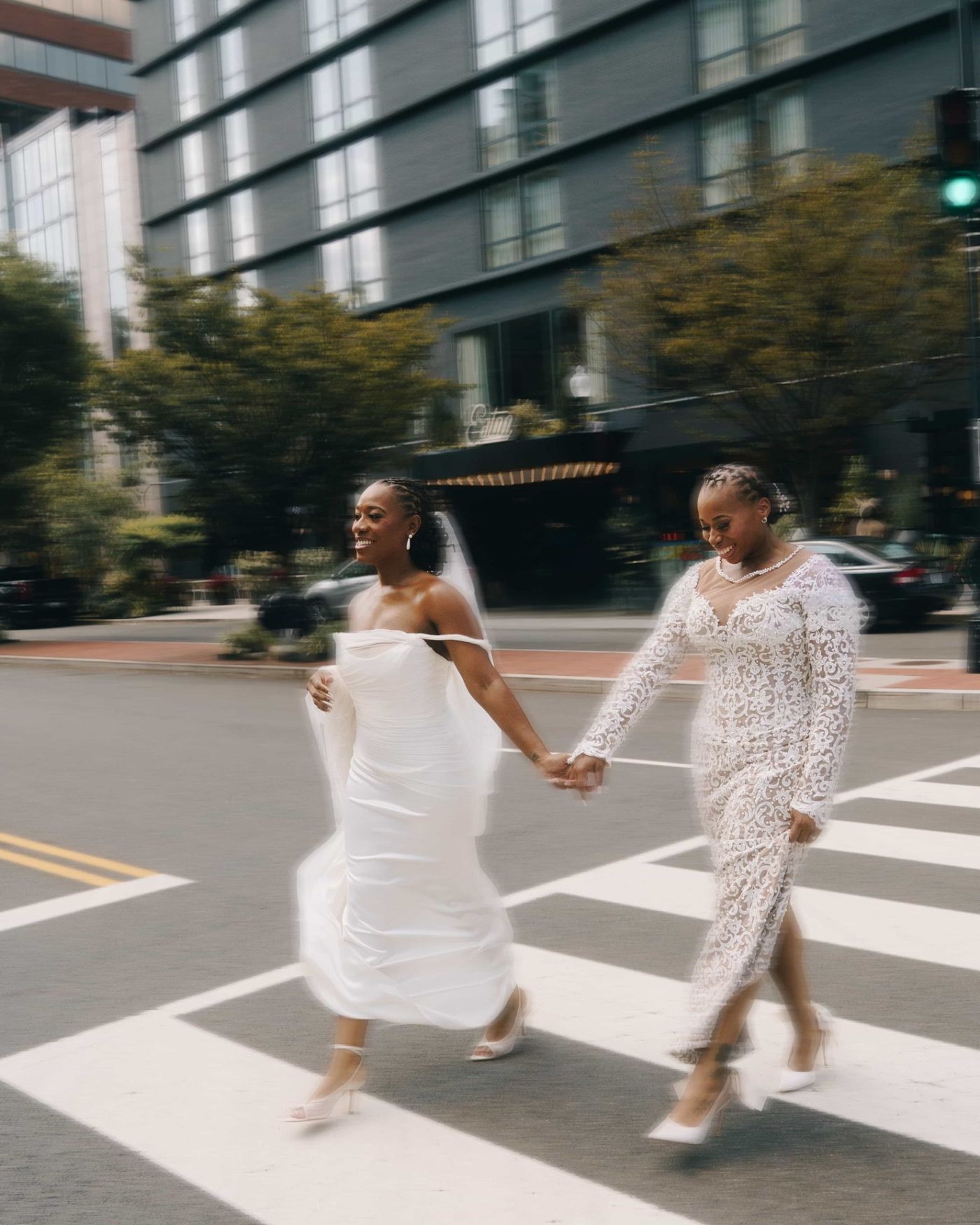 Two brides crossing a city street hand in hand, both blurred with the speed of it