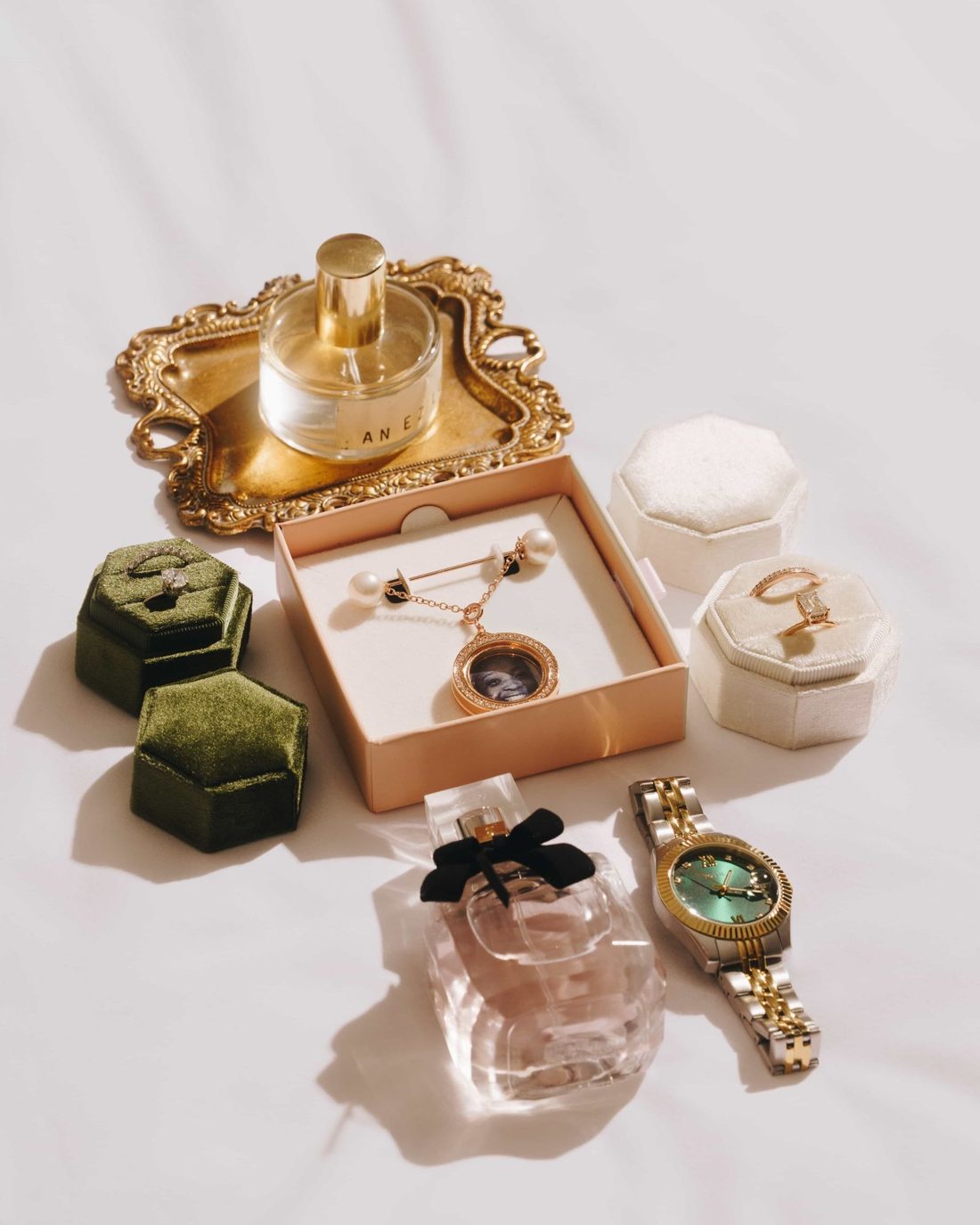 A gold tray of getting ready things: a perfume bottle, a gold watch, a locket and two ring boxes in moss green velvet