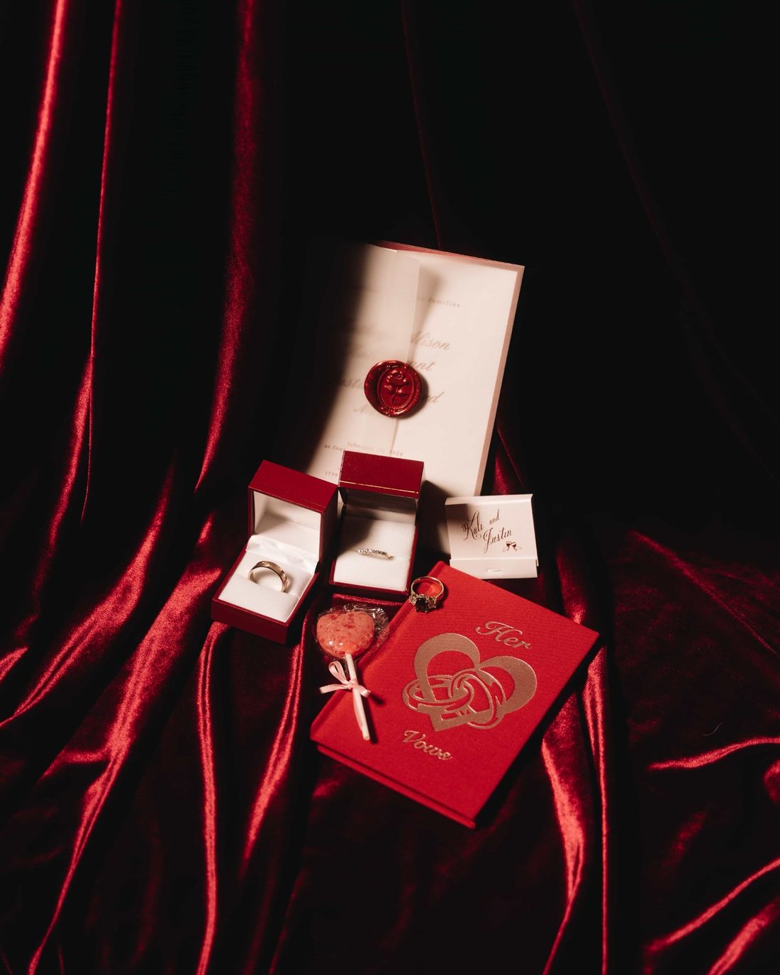 Rings in their boxes on red velvet beside a card printed in gold and a small tasselled knot