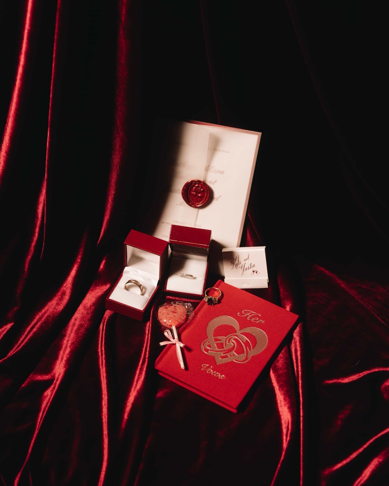 Rings in their boxes on red velvet beside a card printed in gold and a small tasselled knot