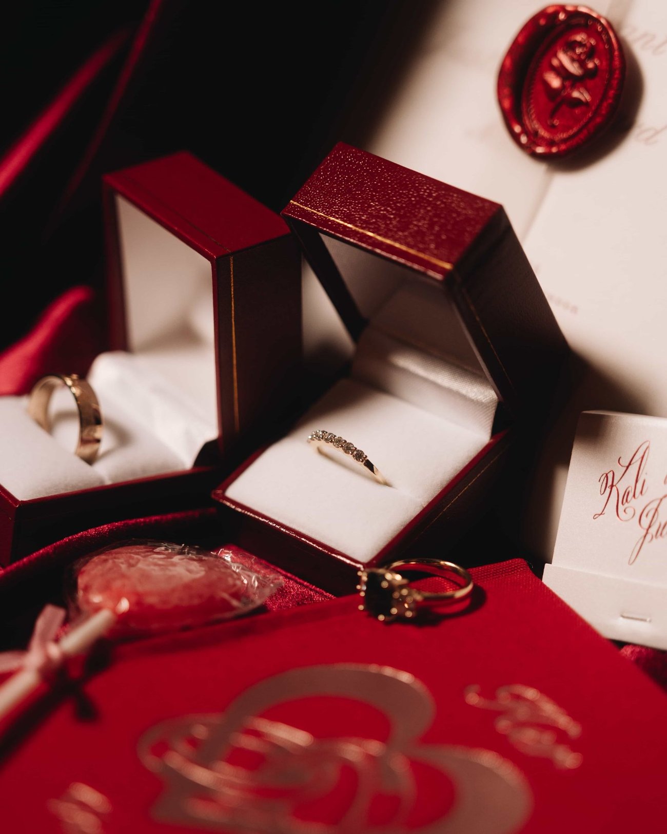 Two gold bands in open boxes on red silk, a round wax seal on the card behind them