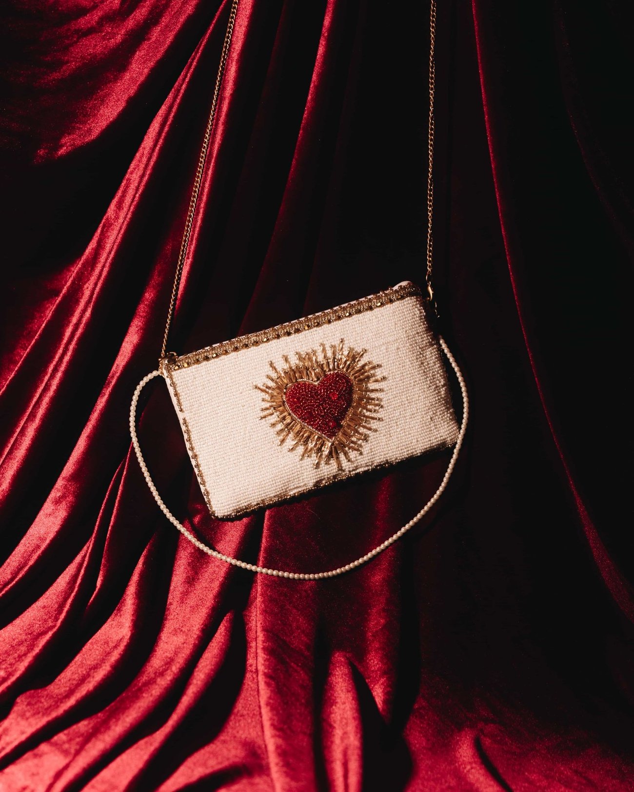 A small beaded purse embroidered with a red heart, hanging by its chain against red velvet
