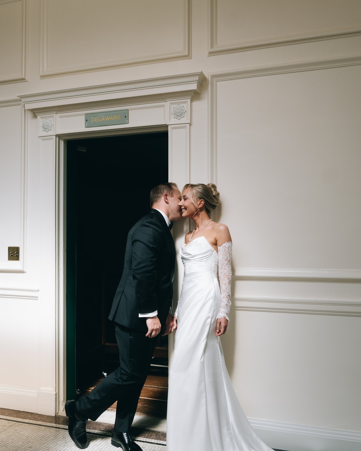 A couple kissing in a panelled doorway, caught between one room and the next