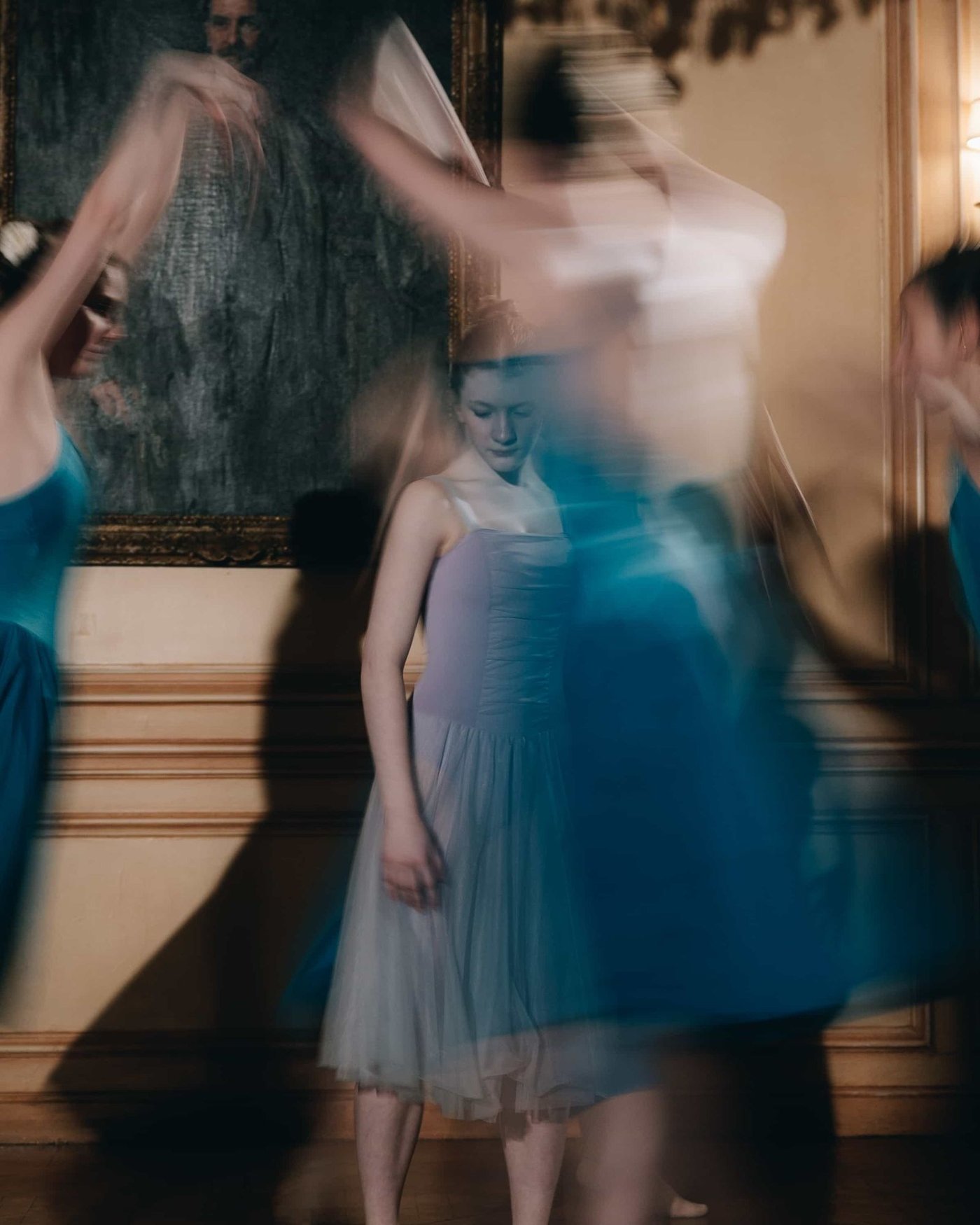 A long exposure of bridesmaids in blue tulle turning together in a grand room