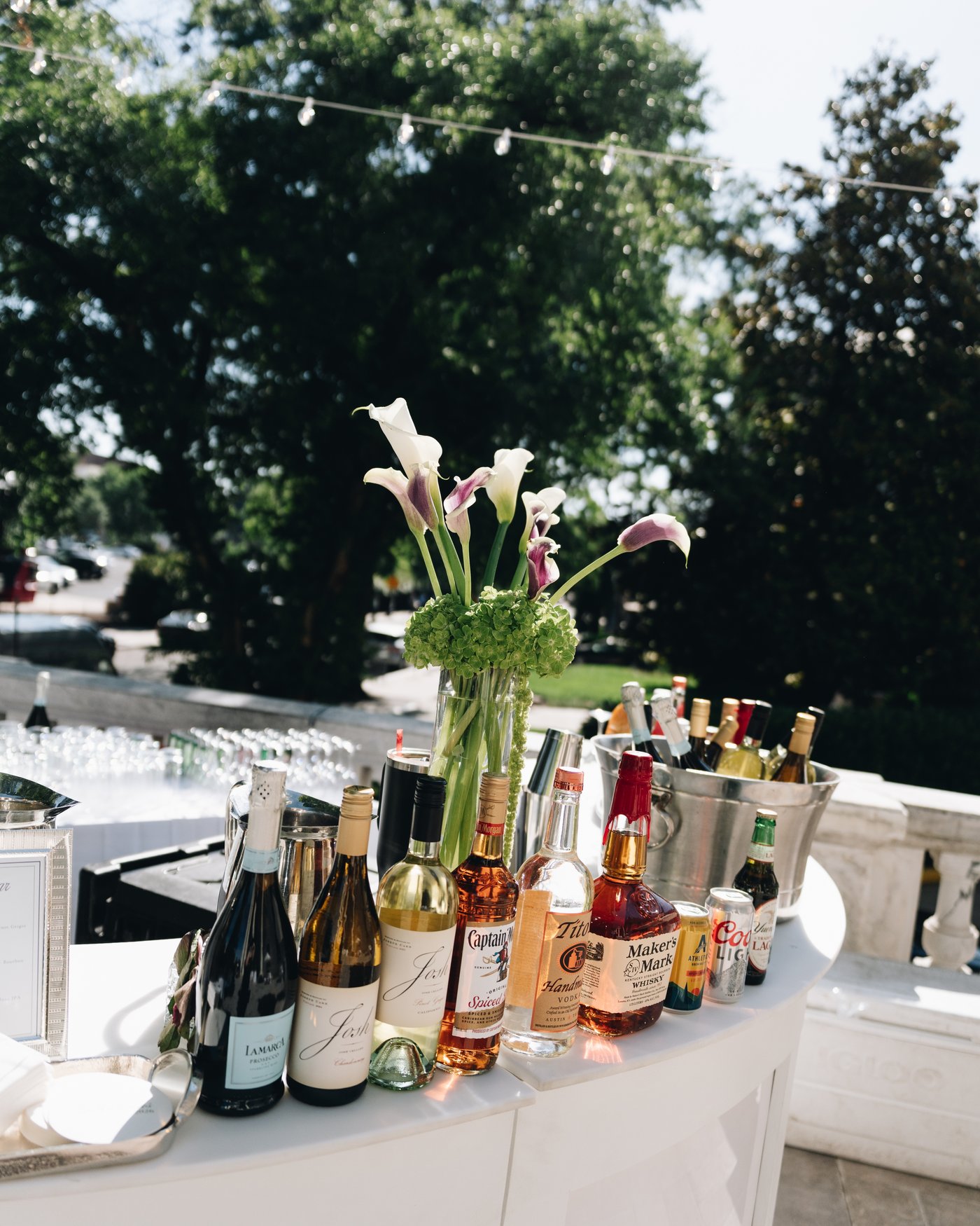 An outdoor bar lined with bottles and ice buckets, calla lilies standing in a vase at the end of it