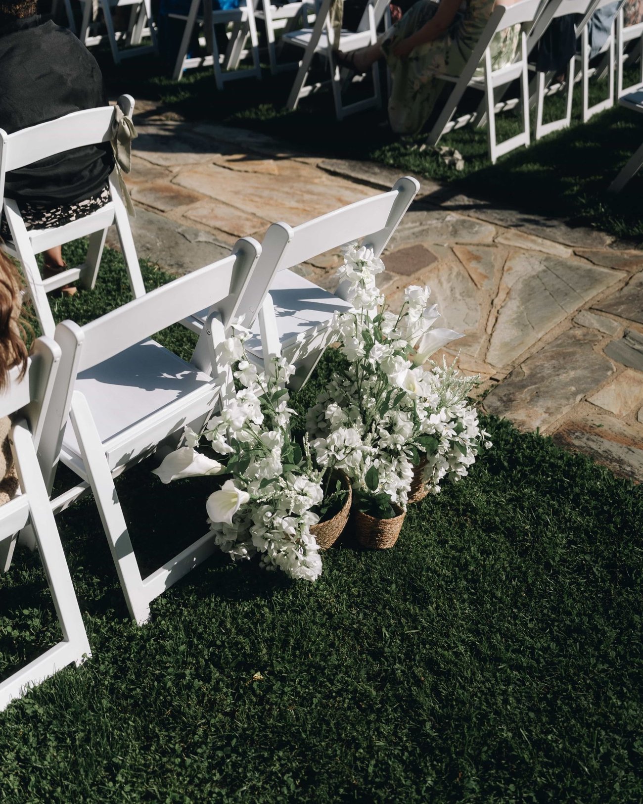 White folding chairs on a flagstone path with a cluster of white flowers marking the end of a row
