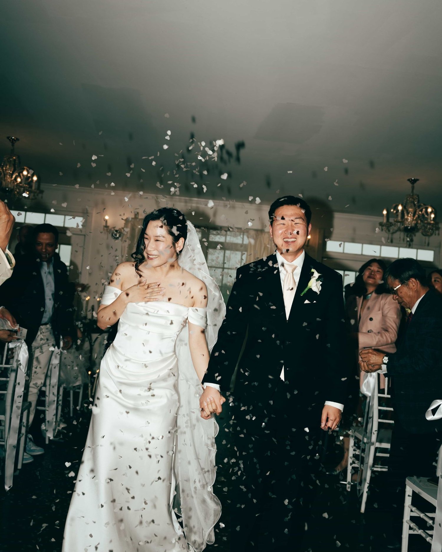 A couple walking back up the aisle through a shower of paper hearts, guests throwing them from both sides